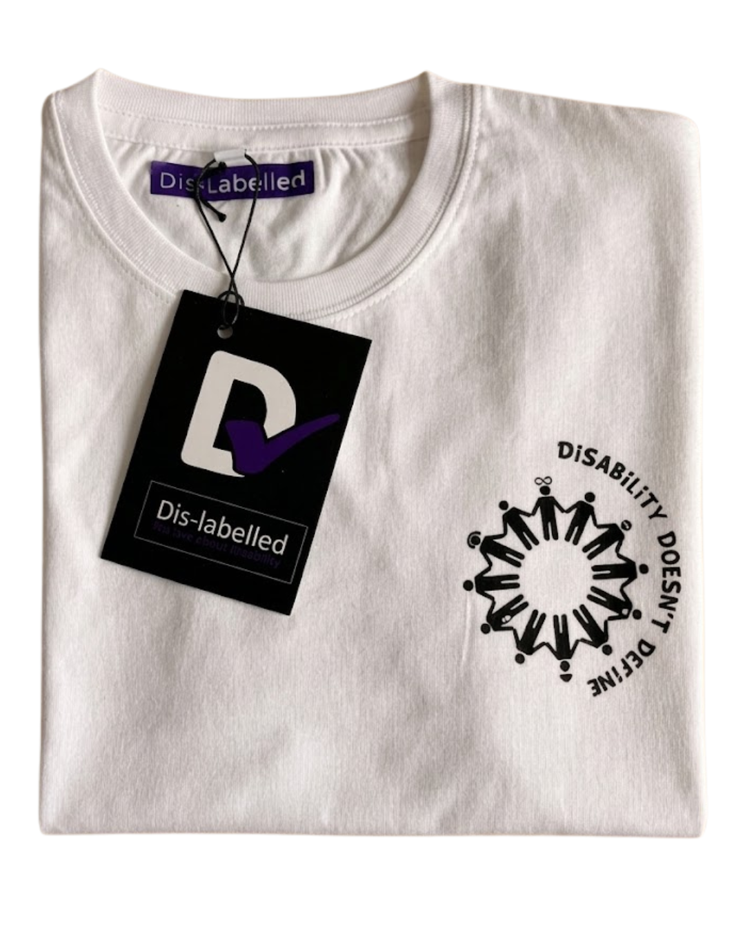 A neatly folded white Dis-Labelled charity t-shirt displayed flat on a light wooden background. The shirt features a black circular logo on the left chest area depicting a ring of stick figures holding hands, surrounded by the text "DiSABILITY DOESN'T DEFINE" in all caps. A black clothing tag with a white 'D' and a purple checkmark hangs from the collar over the upper left chest.